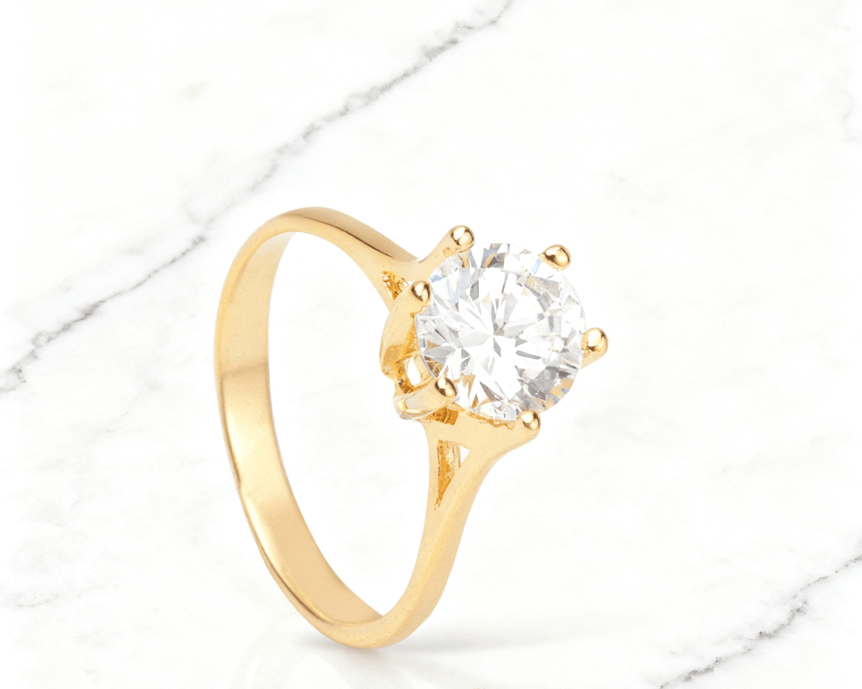 Anel Solitário Dourado com Zircônia Auvane em fundo de mármore claro com veios elegantes