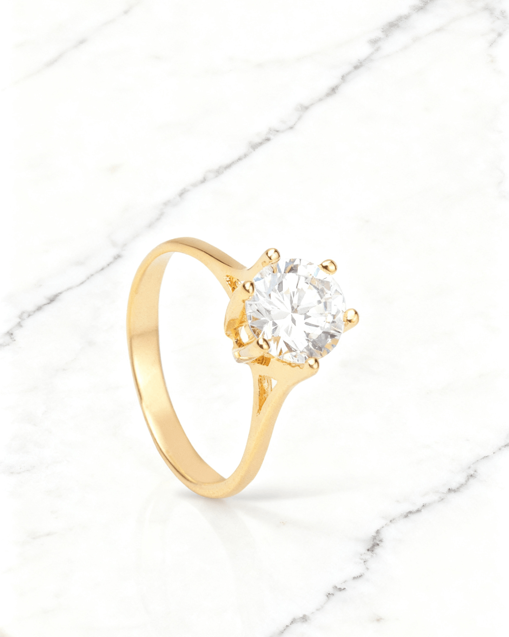 Anel Solitário Dourado com Zircônia Auvane em fundo de mármore claro com veios elegantes