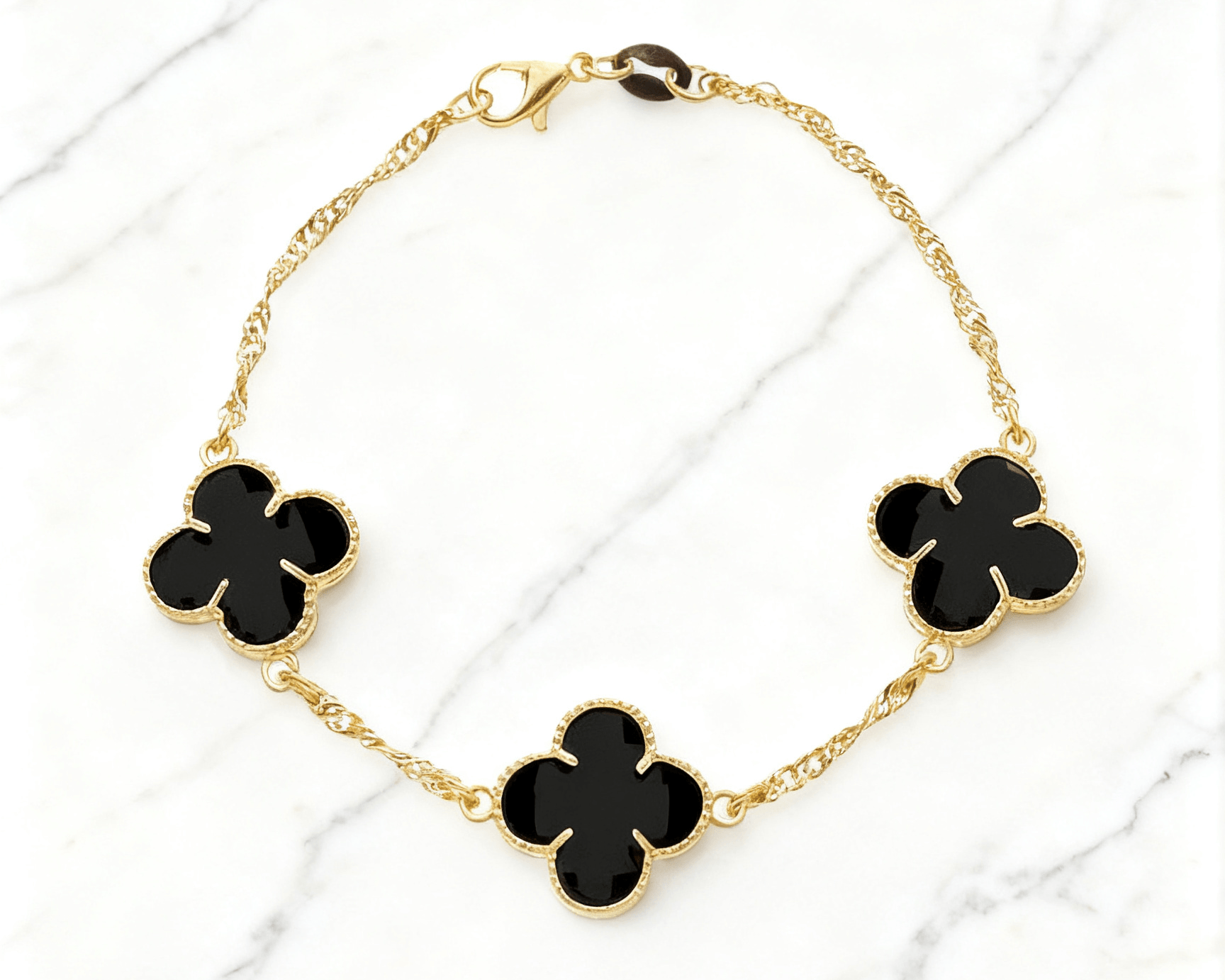 Pulseira Dourada Trevos com Zircônia Preta Auvane em fundo de mármore claro com veios elegantes