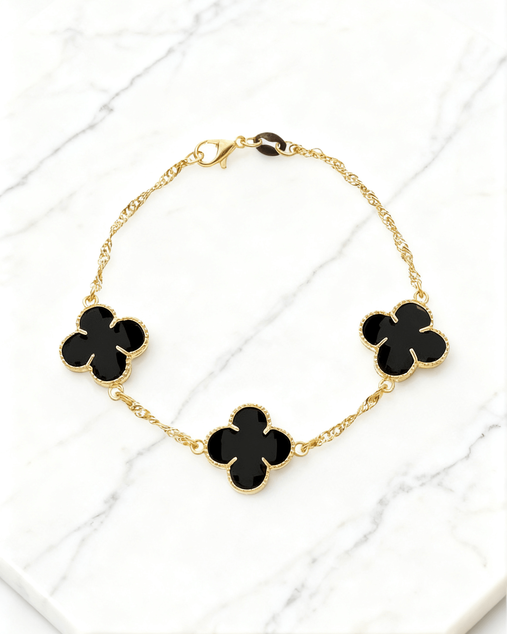 Pulseira Dourada Trevos com Zircônia Preta Auvane em fundo de mármore claro com veios elegantes