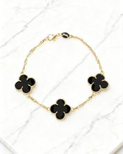 Pulseira Dourada Trevos com Zircônia Preta Auvane em fundo de mármore claro com veios elegantes