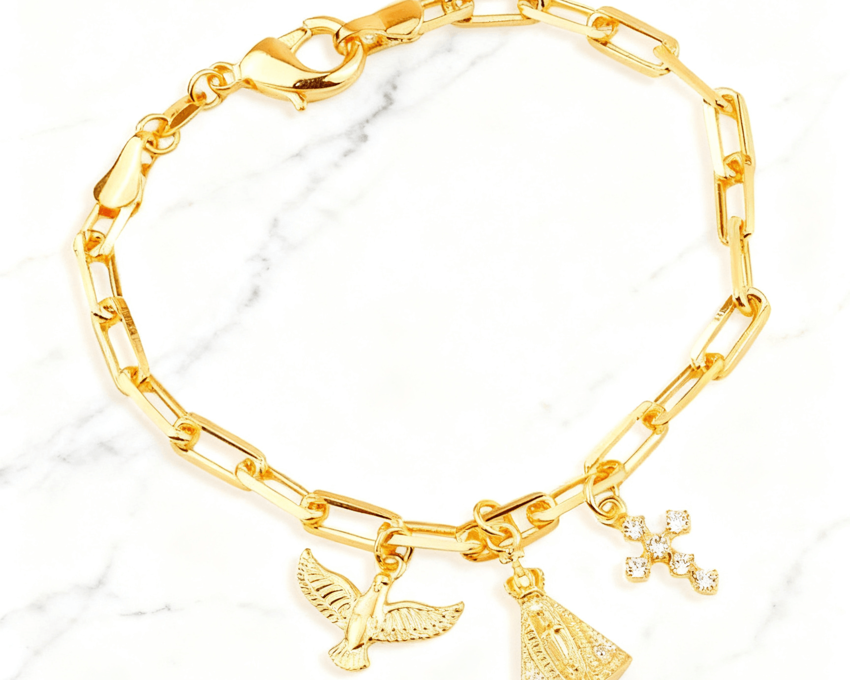 Pulseira Dourada Religiosa Nossa Senhora, Espírito Santo e Cruz Auvane em fundo de mármore claro com veios elegantes