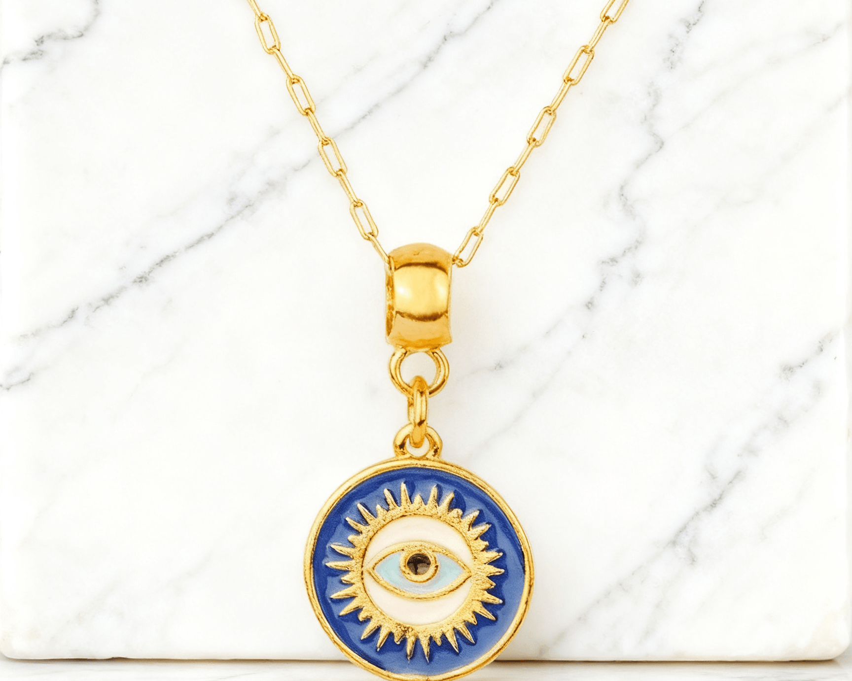 Colar Dourado Medalha Olho Grego Auvane em fundo de mármore claro com veios elegantes