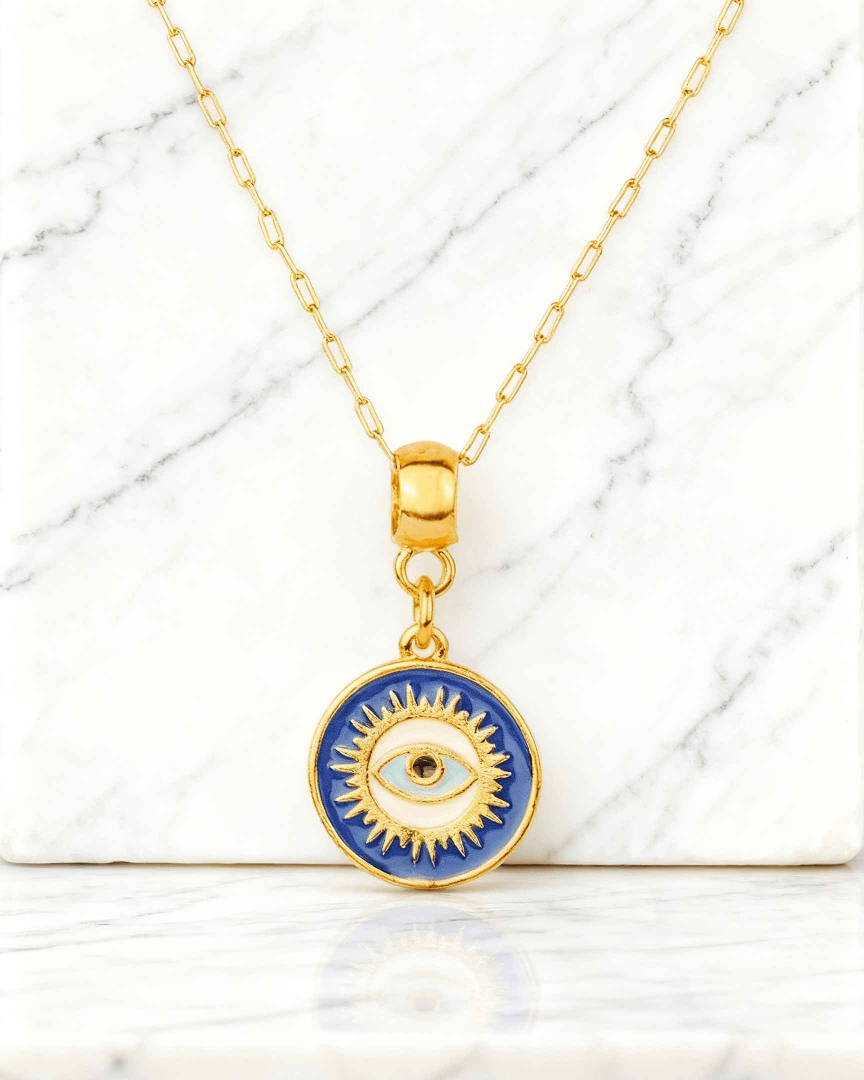 Colar Dourado Medalha Olho Grego Auvane em fundo de mármore claro com veios elegantes