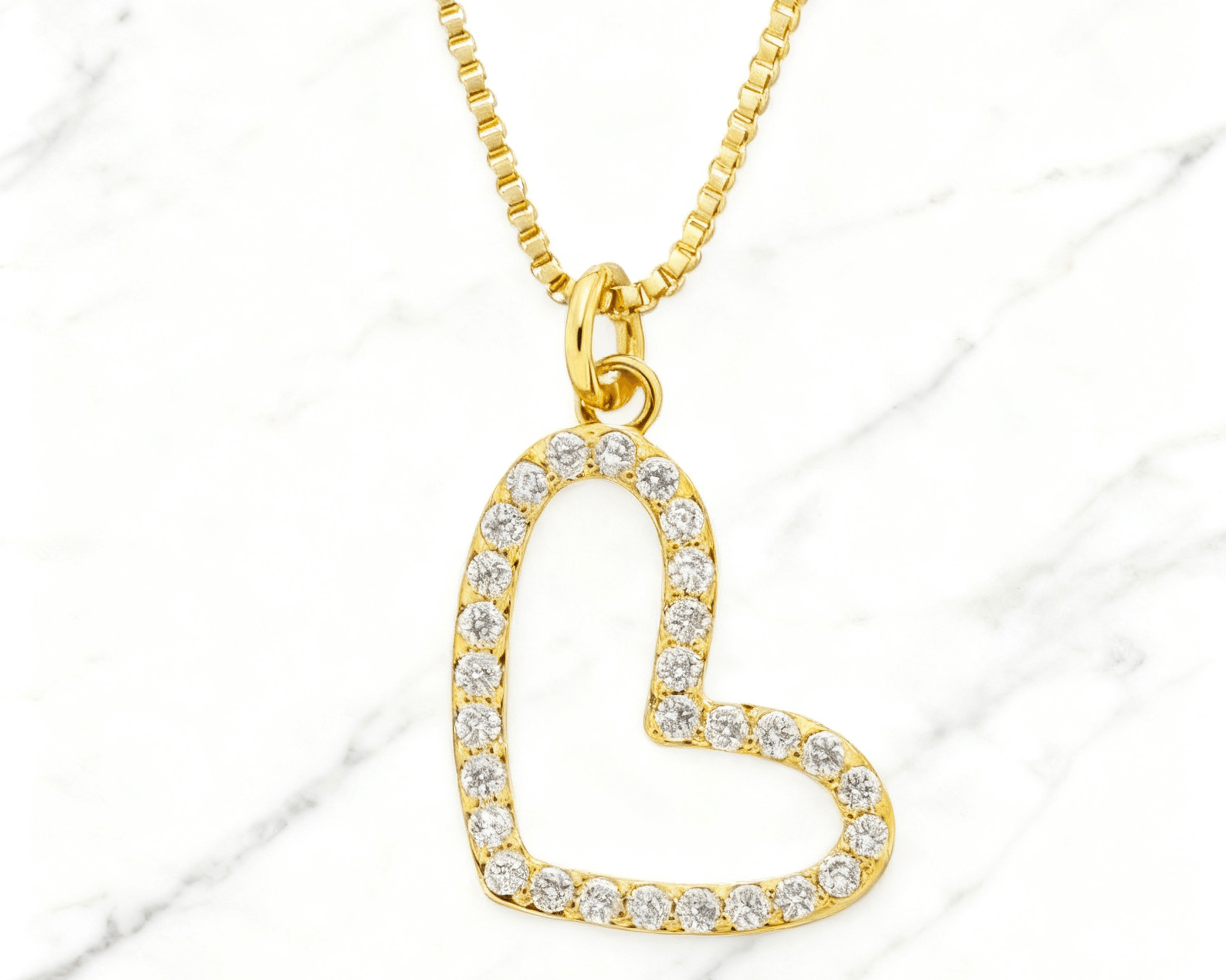 Colar Dourado Coração Vazado com Zircônia Auvane em fundo de mármore claro com veios elegantes