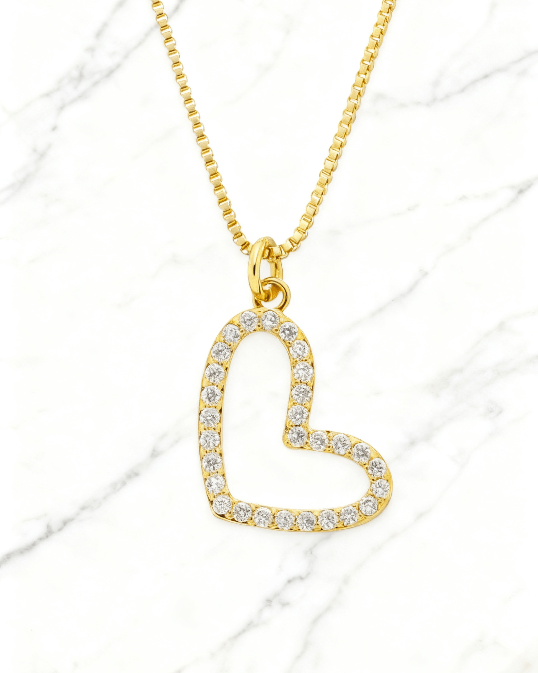 Colar Dourado Coração Vazado com Zircônia Auvane em fundo de mármore claro com veios elegantes