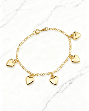 Pulseira Dourada com Pingentes de Coração Auvane em fundo de mármore claro com veios elegantes