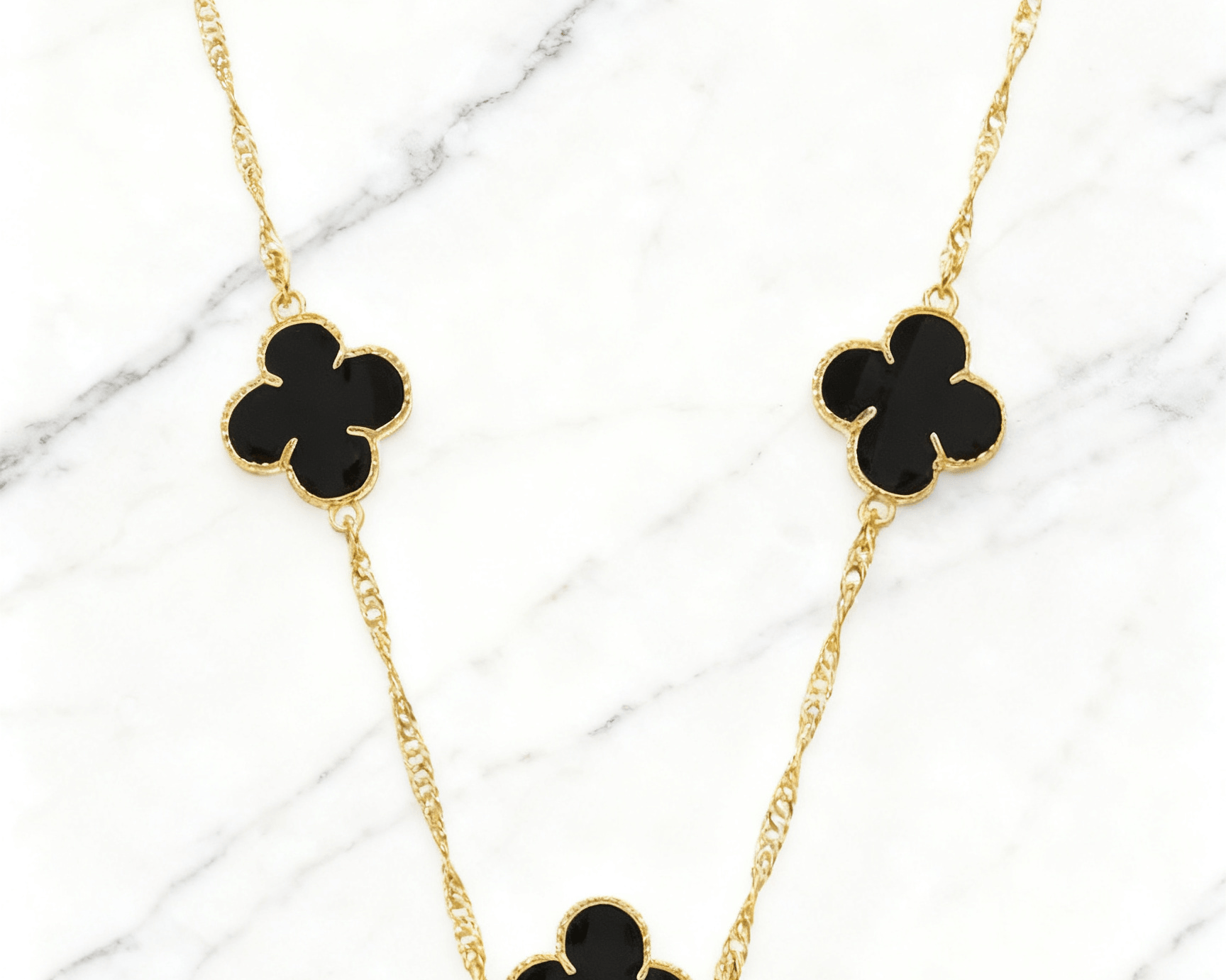 Colar Dourado 5 Trevos Preto Auvane em fundo de mármore claro com veios elegantes