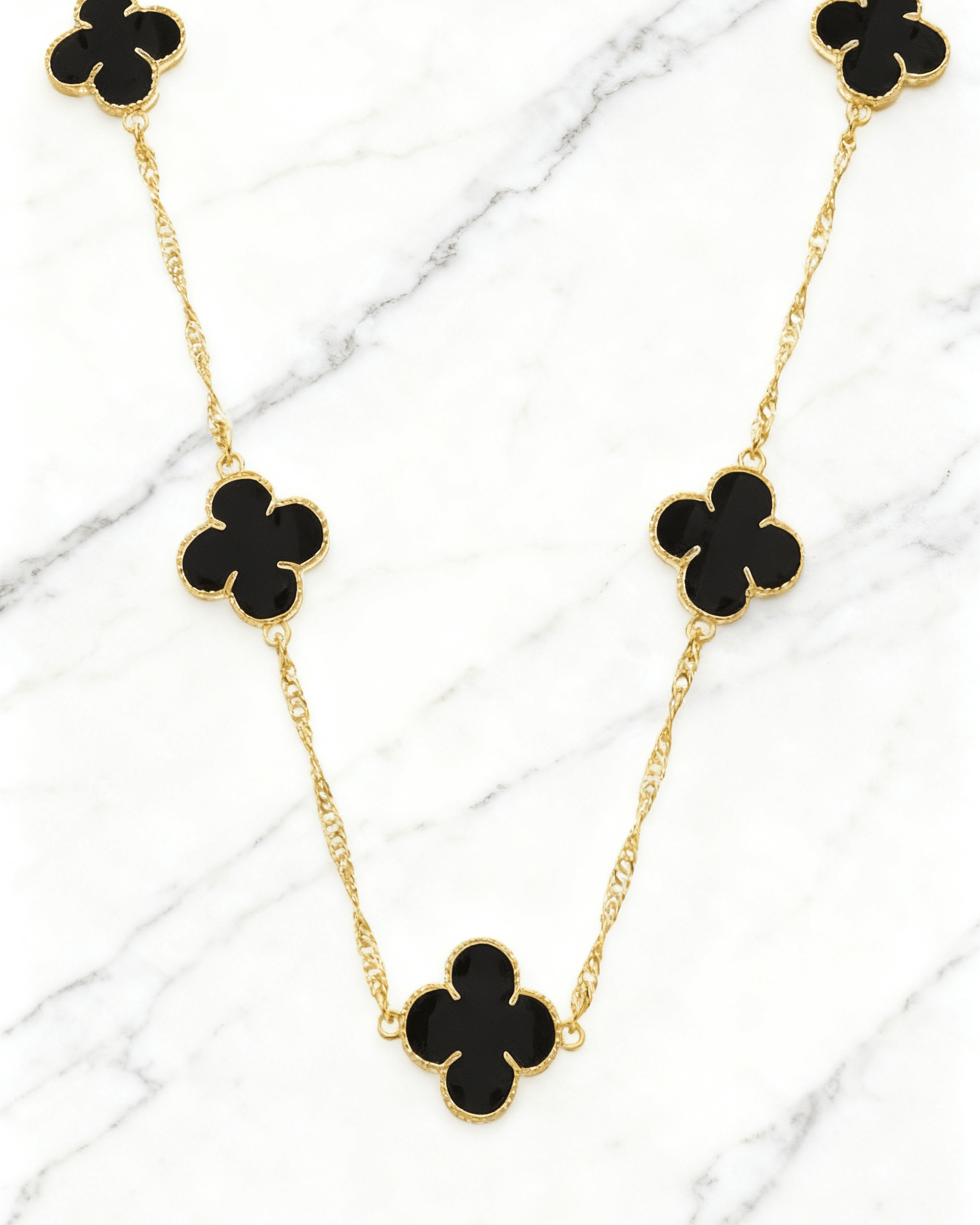 Colar Dourado 5 Trevos Preto Auvane em fundo de mármore claro com veios elegantes