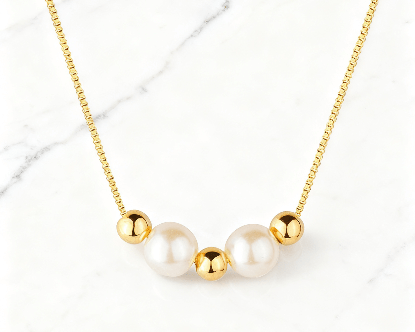 Colar Dourado de Pérolas e Esferas Auvane em fundo de mármore claro com veios elegantes
