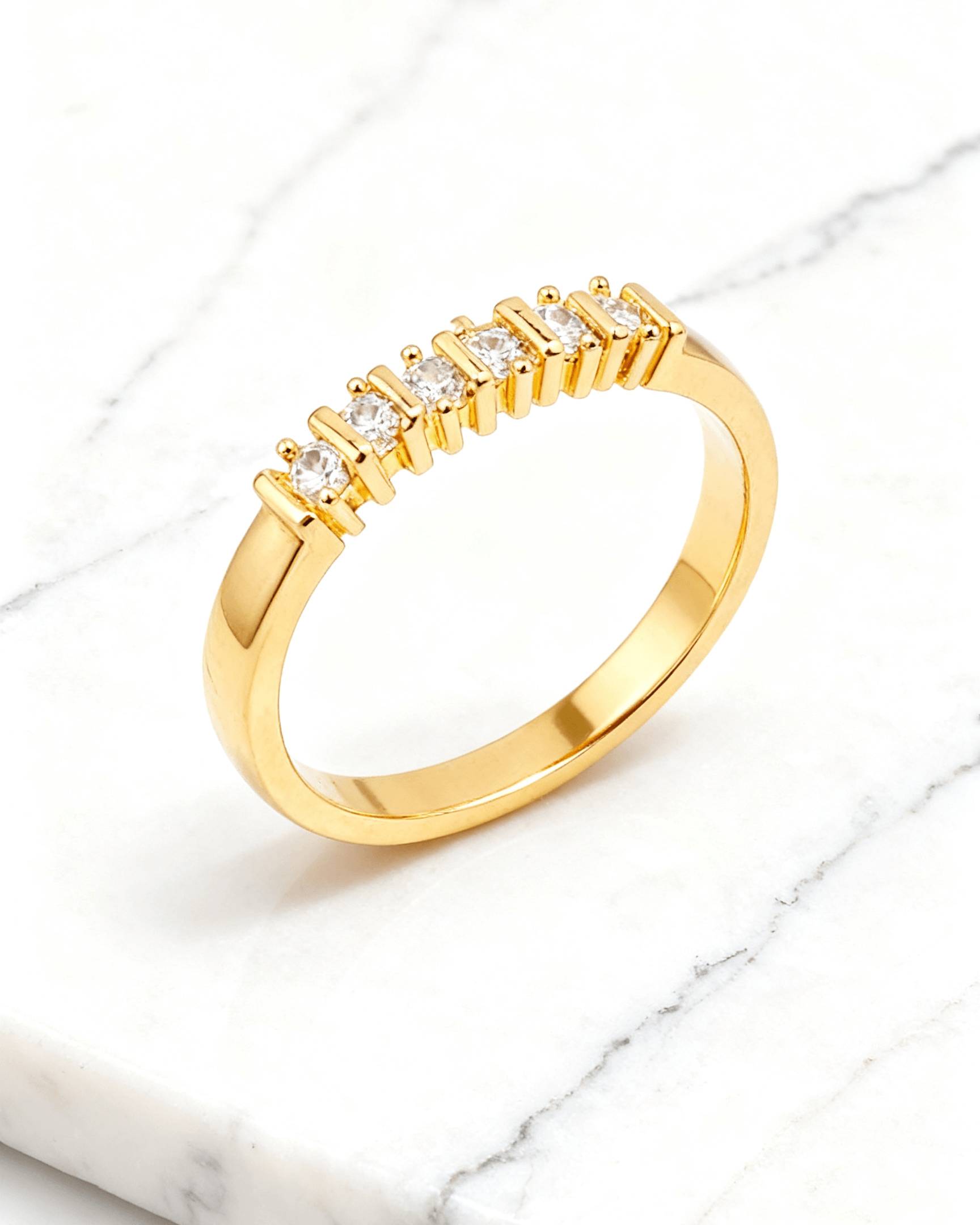 Anel Aparador Dourado de Aliança com 7 Zircônias Auvane em fundo de mármore claro com veios elegantes