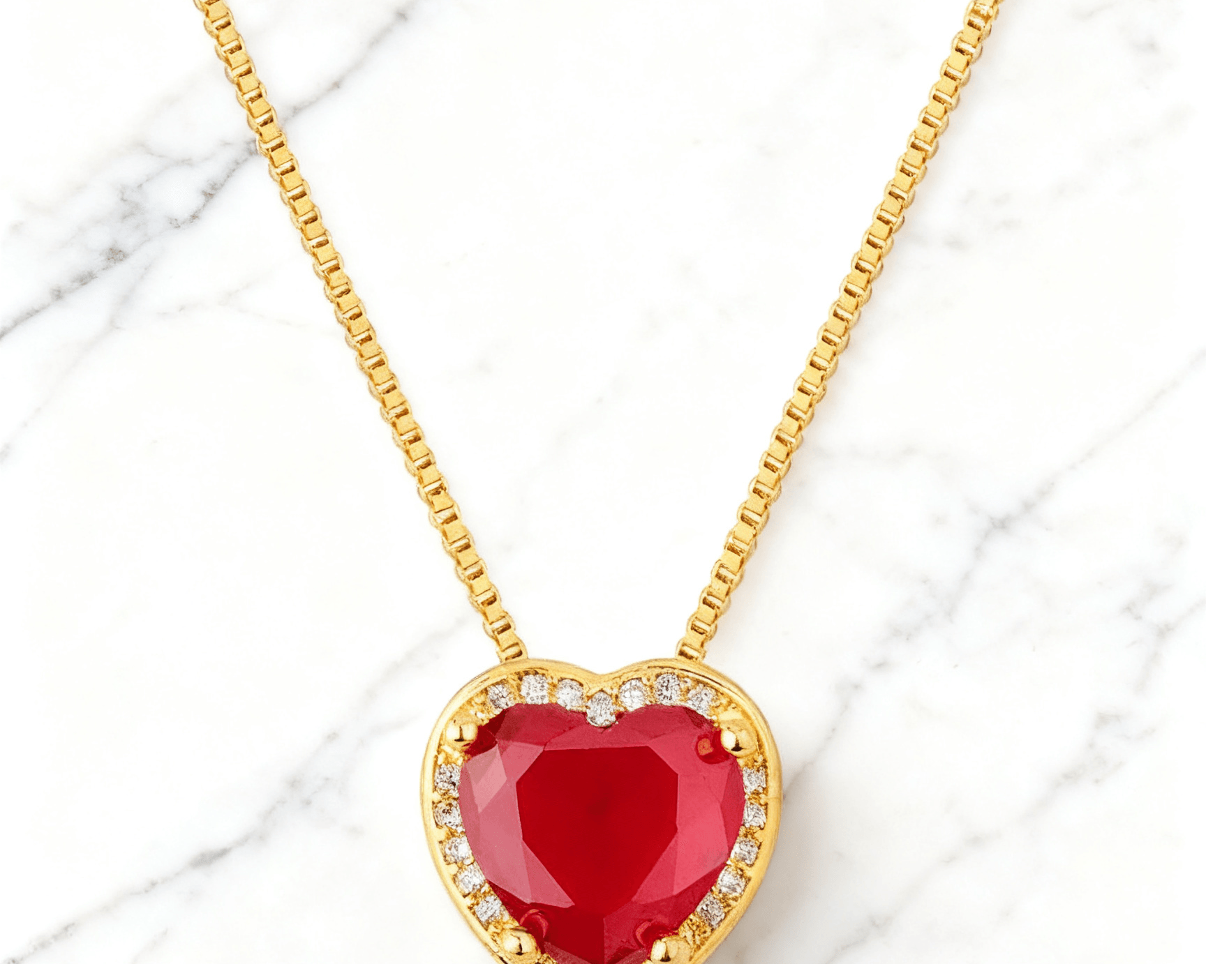 Colar Dourado Coração Vermelho com Zircônias Auvane em fundo de mármore claro com veios elegantes