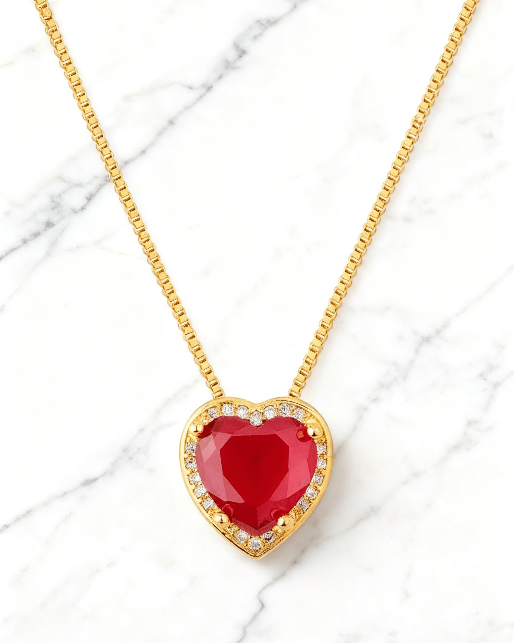 Colar Dourado Coração Vermelho com Zircônias Auvane em fundo de mármore claro com veios elegantes