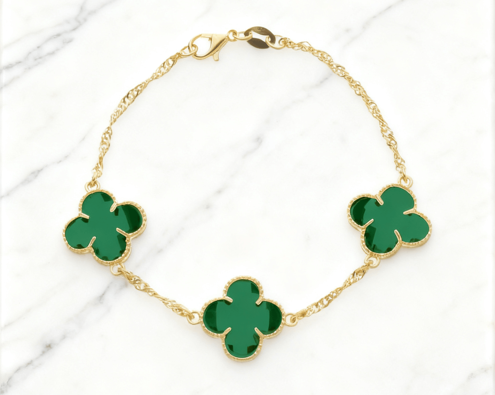 Pulseira Dourada Trevos com Zircônia Verde Auvane em fundo de mármore claro com veios elegantes
