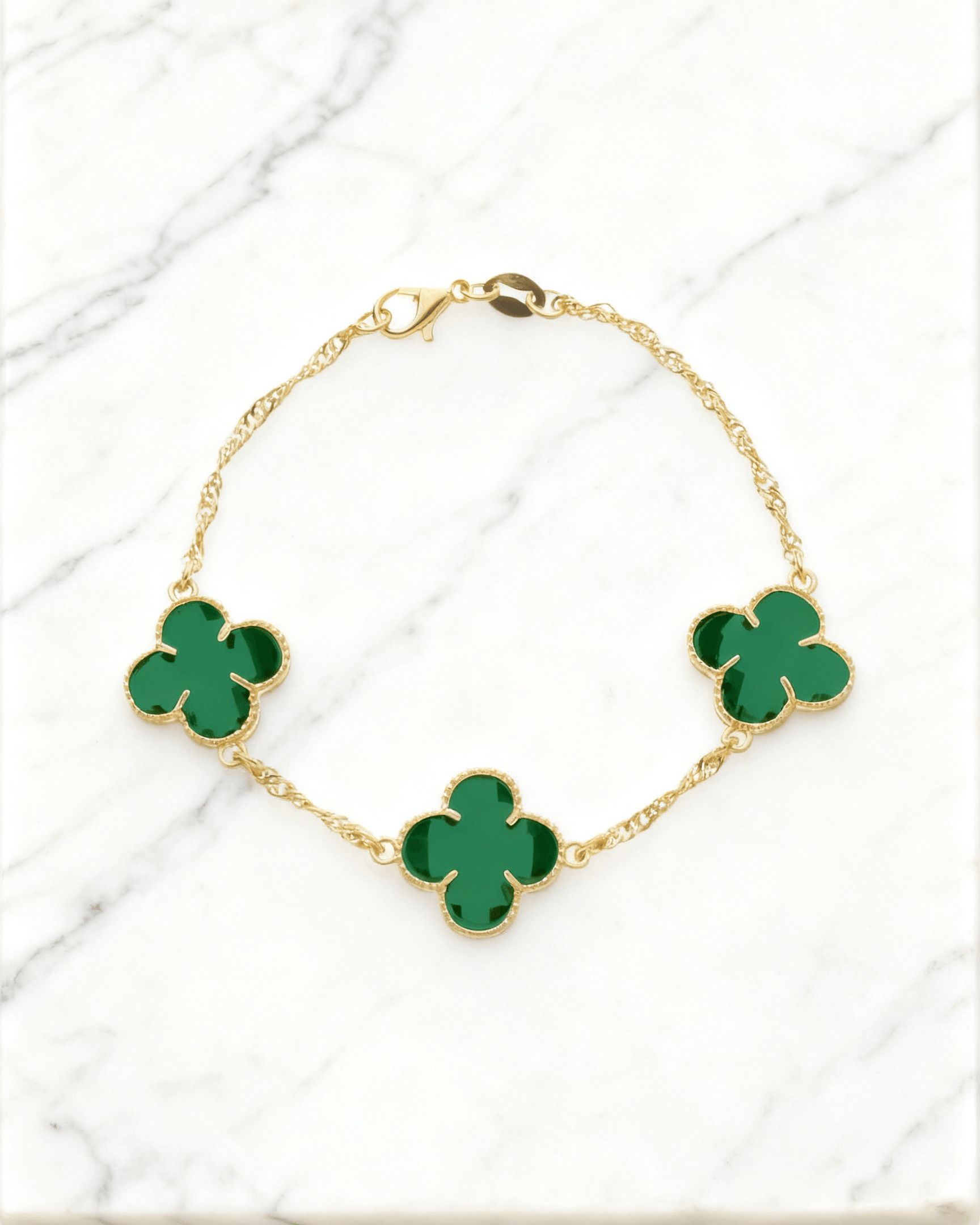 Pulseira Dourada Trevos com Zircônia Verde Auvane em fundo de mármore claro com veios elegantes