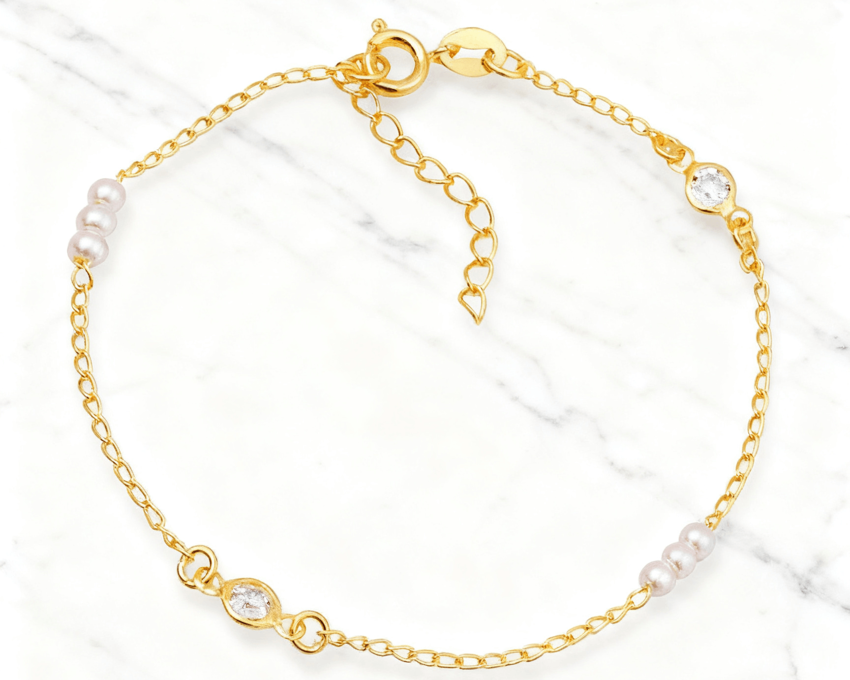 Pulseira Dourada de Pérolas com Ponto de Luz Auvane em fundo de mármore claro com veios elegantes