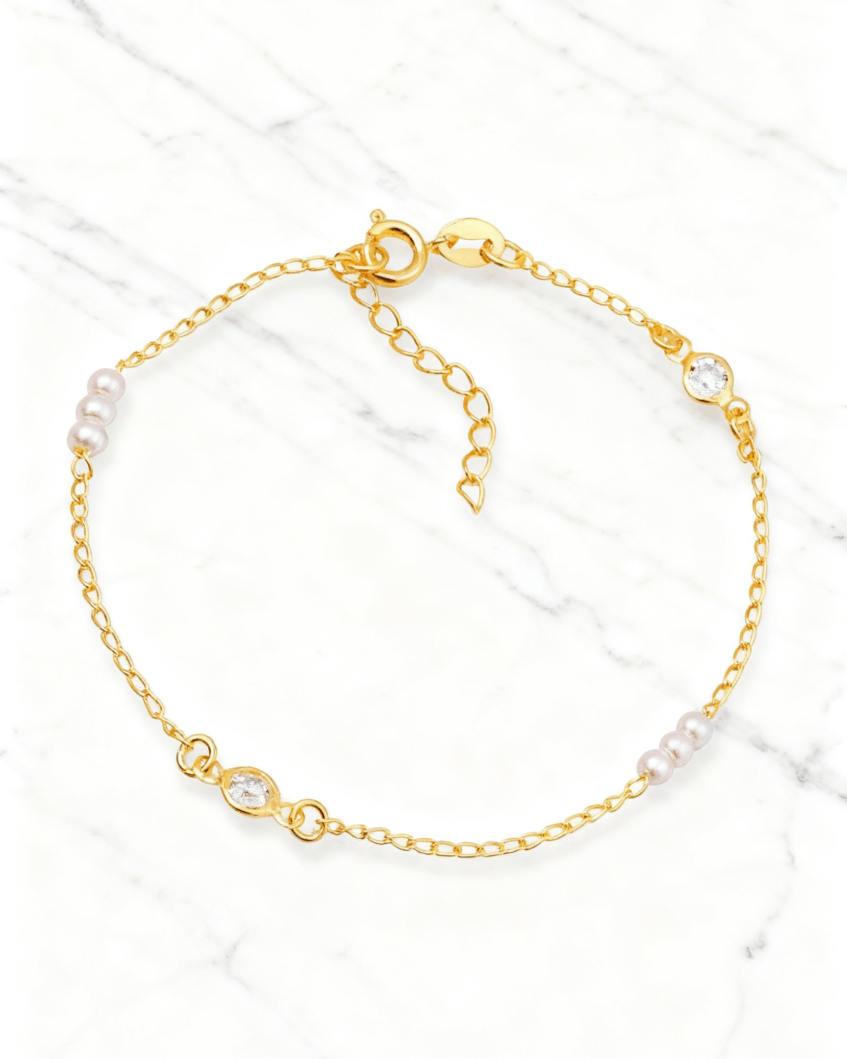 Pulseira Dourada de Pérolas com Ponto de Luz Auvane em fundo de mármore claro com veios elegantes