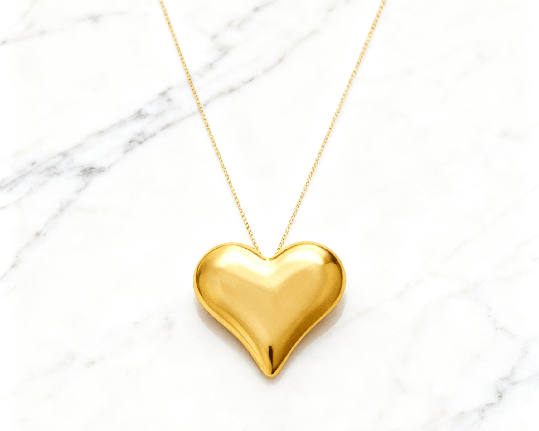 Colar Dourado de Coração Liso Auvane em fundo de mármore claro com veios elegantes