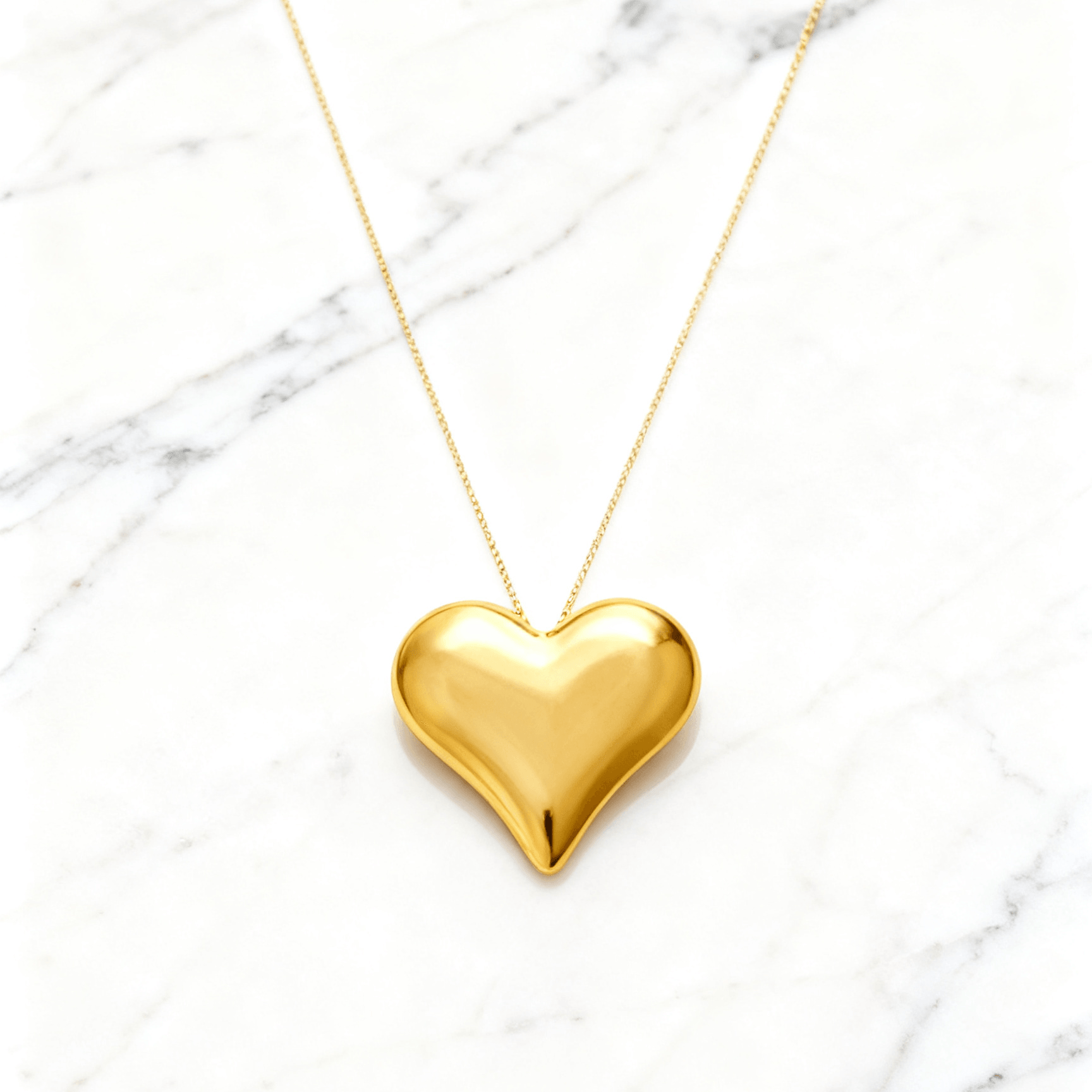 Colar Dourado de Coração Liso Auvane em fundo de mármore claro com veios elegantes