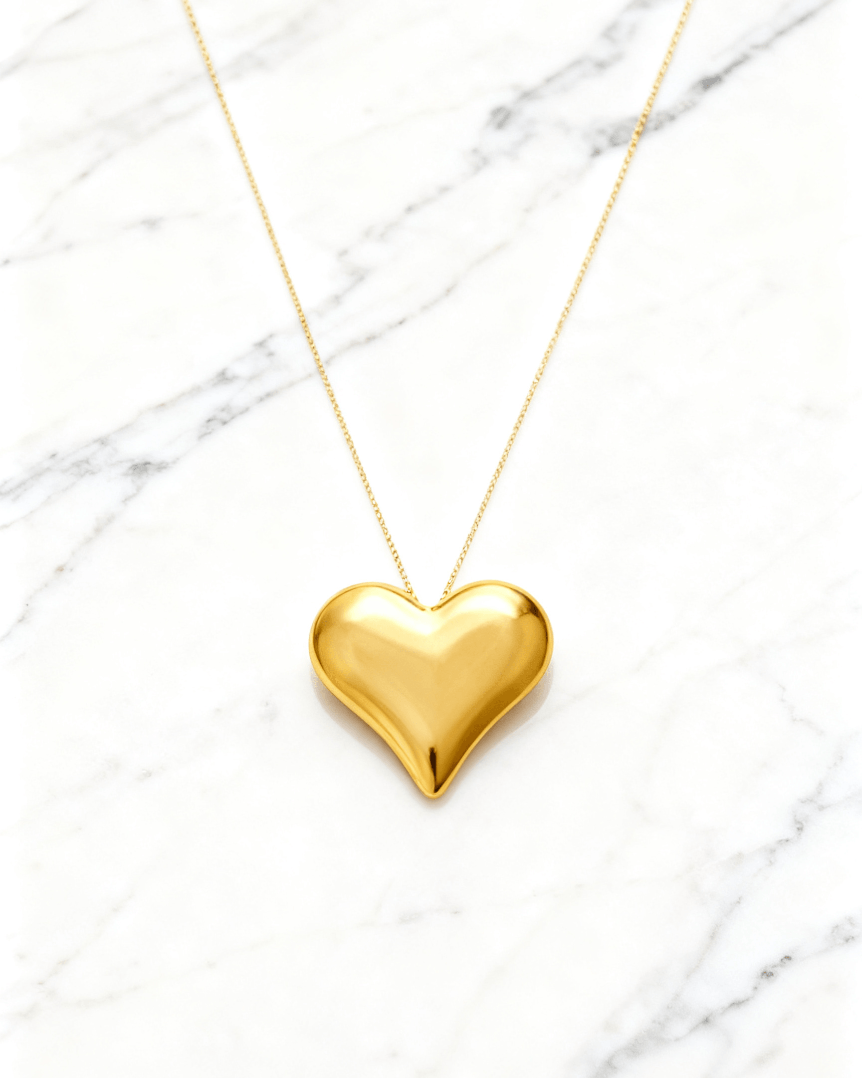 Colar Dourado de Coração Liso Auvane em fundo de mármore claro com veios elegantes