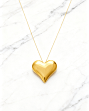 Colar Dourado de Coração Liso Auvane em fundo de mármore claro com veios elegantes