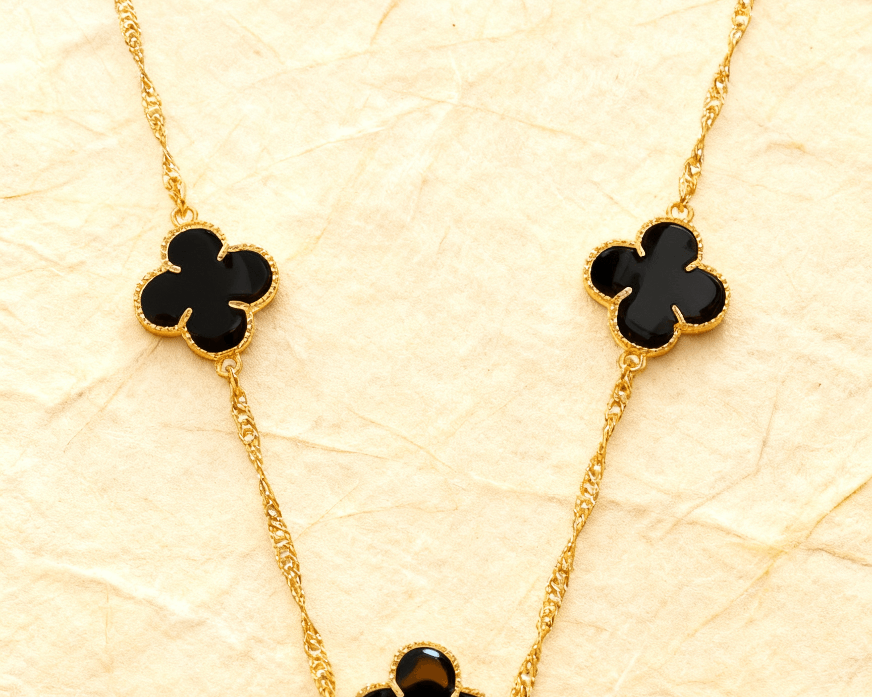 Colar Dourado 5 Trevos Preto Auvane sobre papel artesanal cream